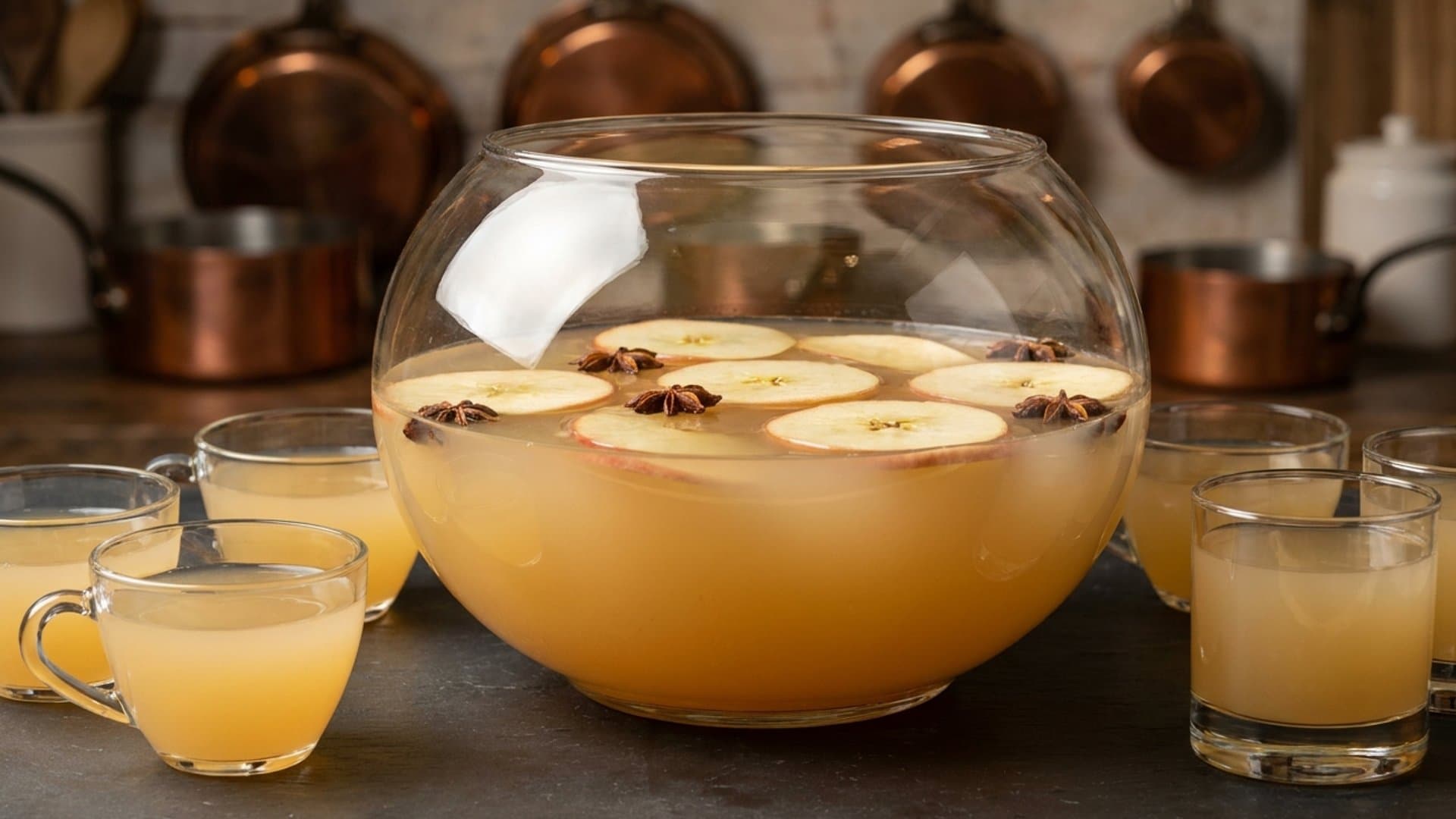 Harvest Moon Punch cocktail in a punch bowl with punch cups or rocks glasses garnished with thin apple slices and star anise pods