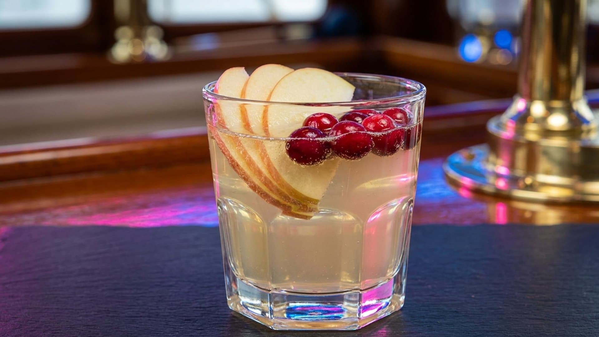 Harvest Moon Punch cocktail in a punch cup or rocks glass garnished with Fresh apple slices and cranberries floated on top